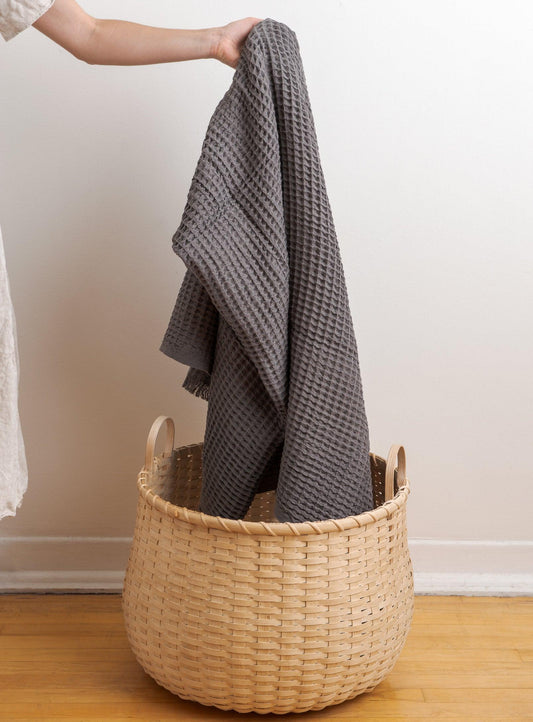 woman putting a grey blanket into a basket on the floor