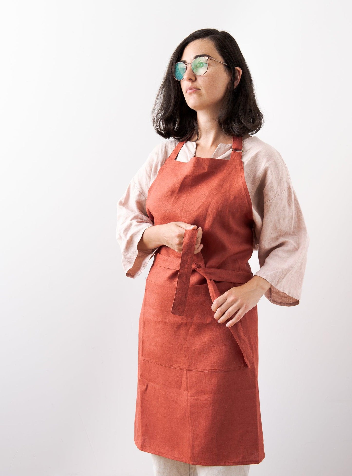 woman with pink linen shirt tying a red apron