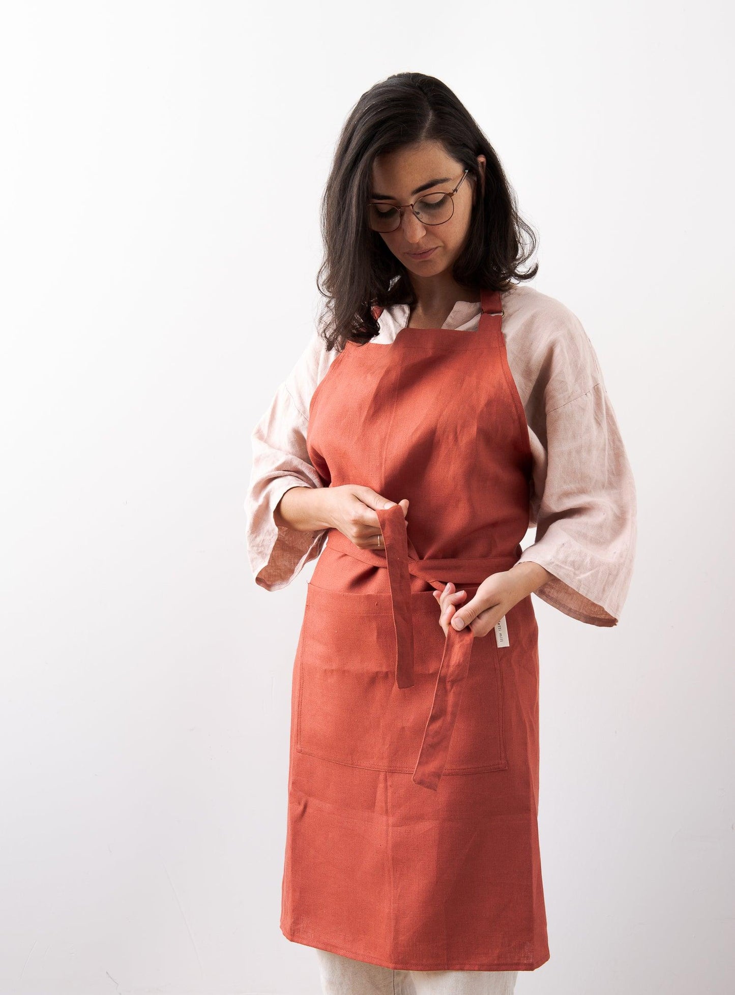 woman tying a red apron in front of a white wall