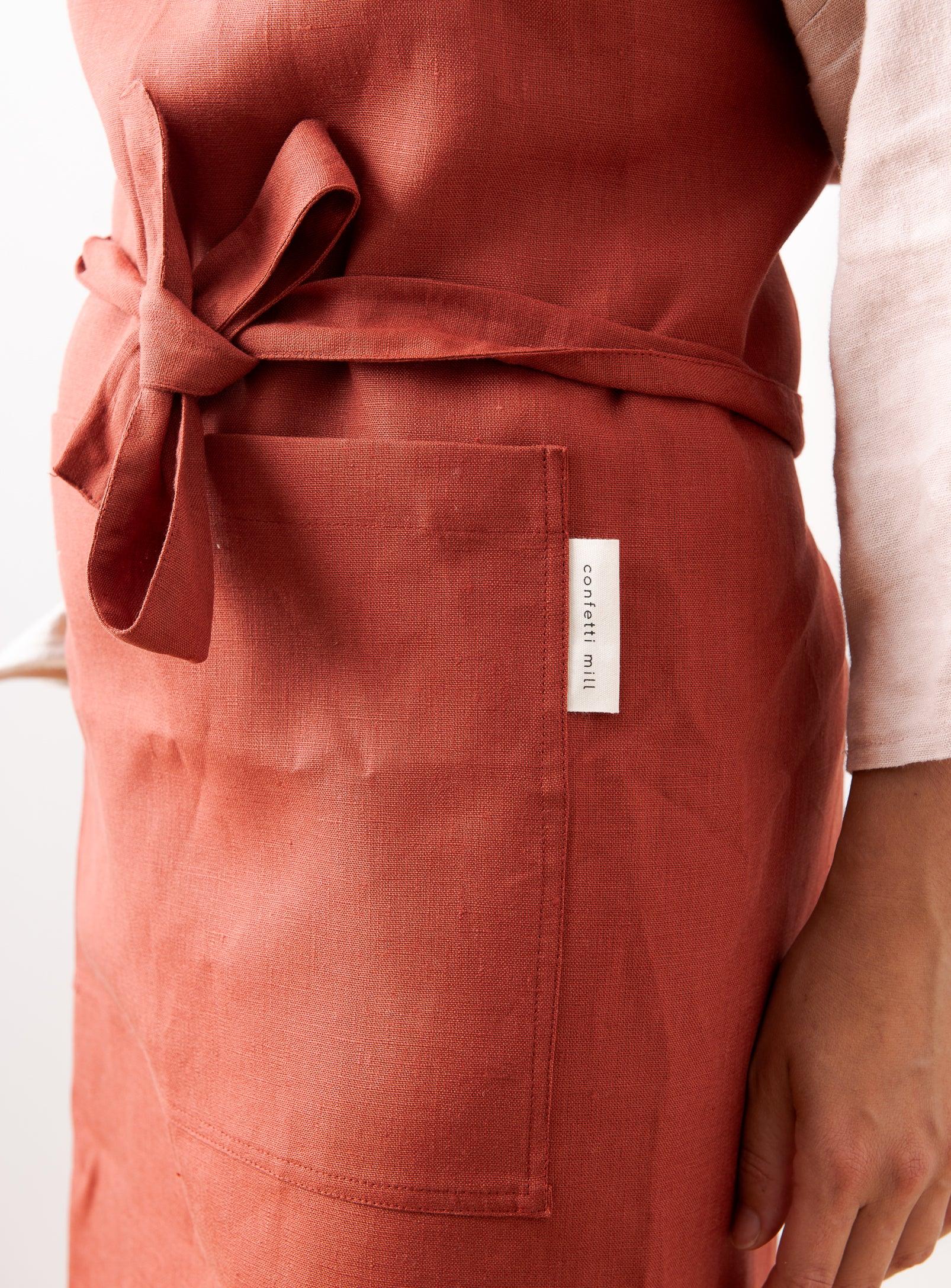 a detailed view of a red linen apron where we see the brand name tag confetti mill