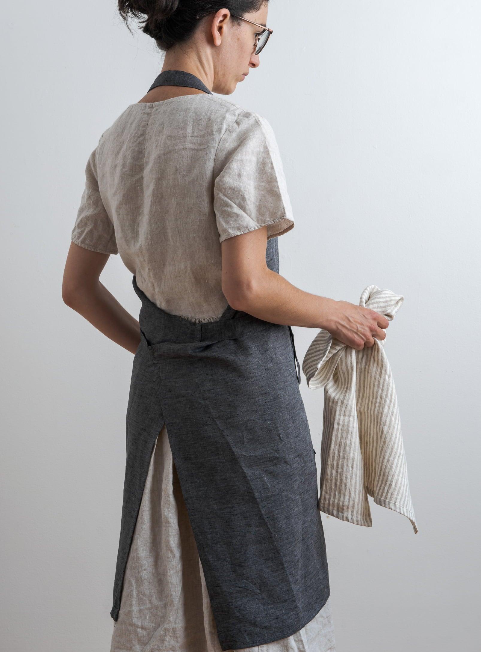 woman seen from behind wearing a grey kitchen apron and holding a tea towel