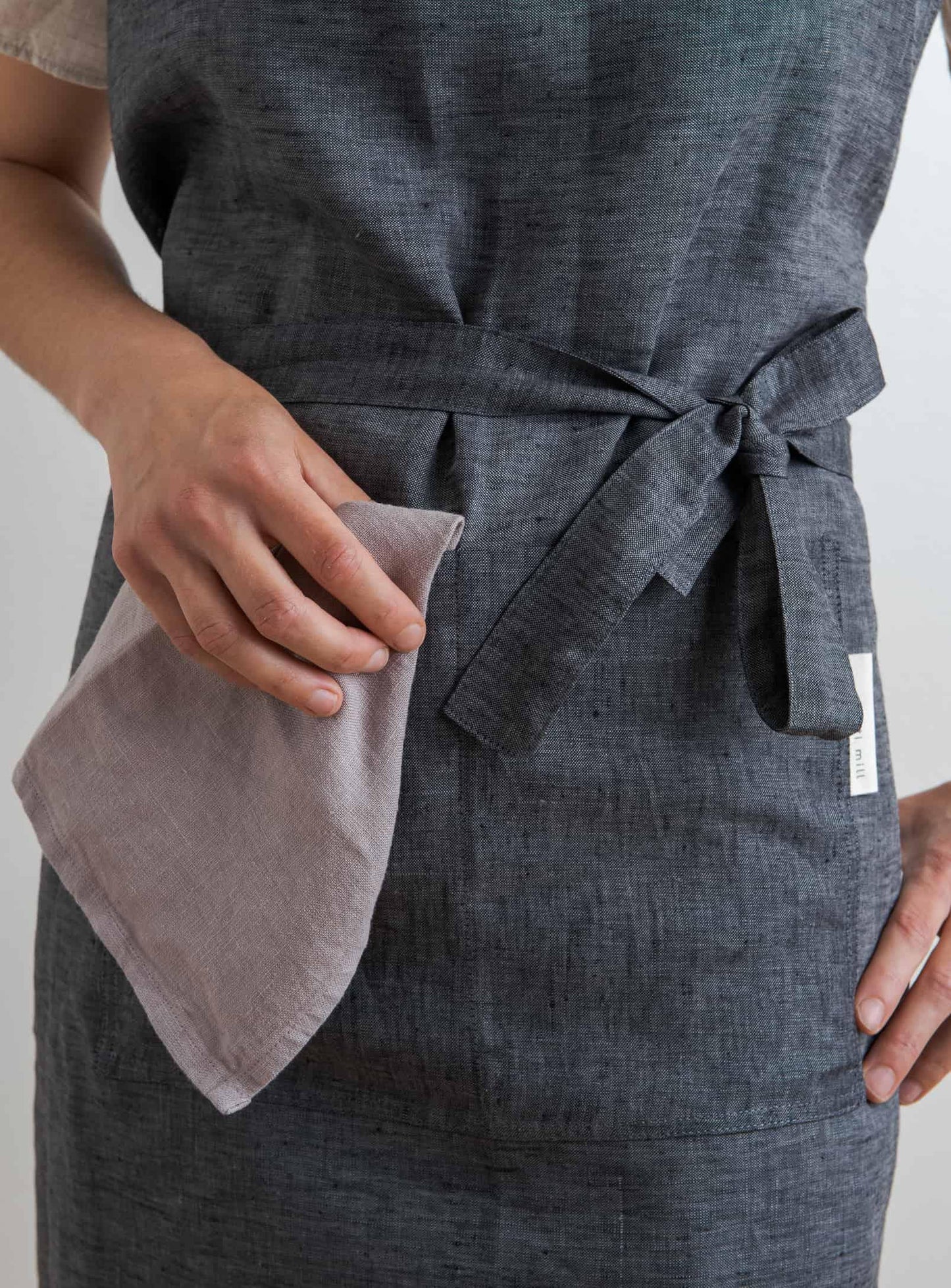 front view of a woman wearing an anthracite coloured kitchen apron holding a dinner napkin