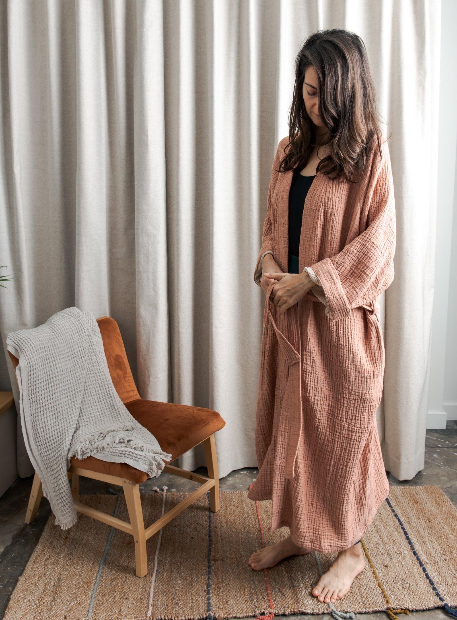 woman wearing a pink cotton robe, loungewear next to an armchair